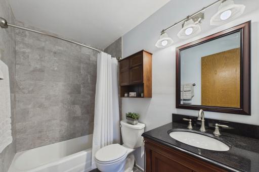 Updated full bathroom featuring attractive tile tub surround, dark vanity with stone countertop, and stylish fixtures.