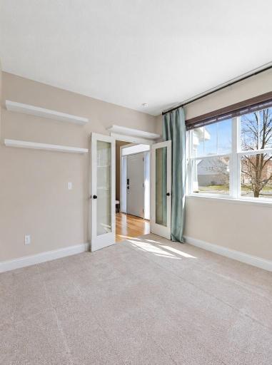 Versatile office space featuring abundant natural light, French doors, built-in floating shelves, and ample room to create a comfortable workspace.
