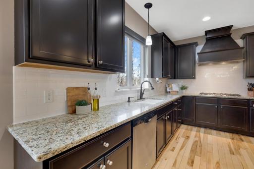 A beautifully appointed kitchen features rich cabinetry, granite countertops, a classic subway tile backsplash, stainless steel dishwasher, and abundant natural light from the window above the sink