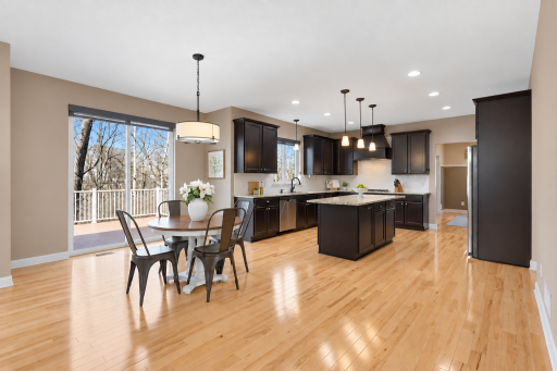 Spacious open-concept kitchen and dining area featuring rich cabinetry, granite countertops, stainless steel appliances, a large center island, and gleaming hardwood floors, with expansive windows and sliding doors bringing in abundant natural light