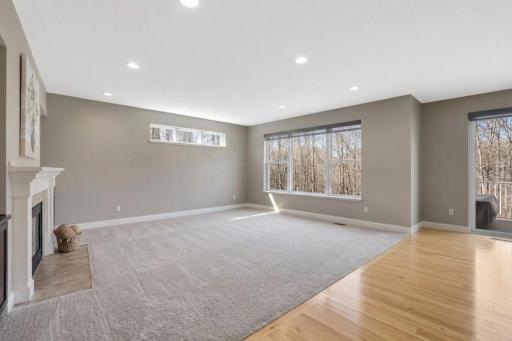 Bright, versatile living area offers generous space, large windows overlooking the wooded setting, a cozy fireplace, and easy access to the deck.