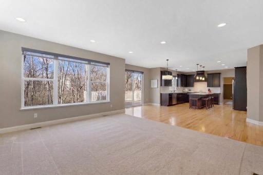 Spacious open-concept living area showcases expansive windows with peaceful wooded views, abundant natural light, and a seamless flow into the kitchen and dining spaces, complemented by warm hardwood floors and convenient deck access.