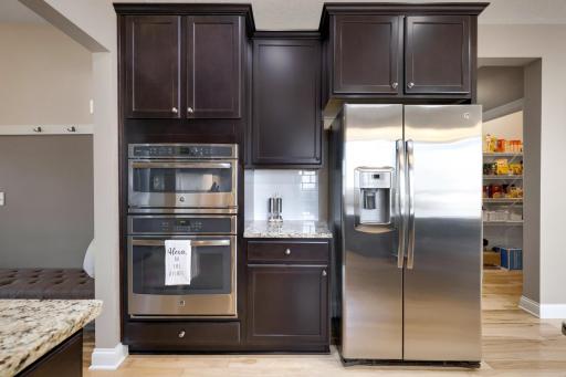 The kitchen features rich cabinetry, stainless steel appliances, built-in microwave and oven, granite countertops, and convenient access to the walk-in pantry