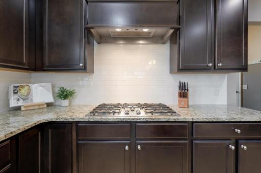 The spacious cooking area showcases a gas cooktop, custom range hood, granite countertops, subway tile backsplash, and generous cabinetry for storage