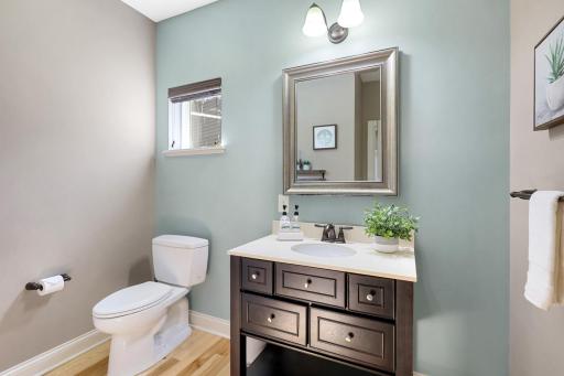 Inviting powder room features a stylish vanity, coordinating fixtures, hardwood flooring, and a soft accent wall, complemented by natural light for a bright and welcoming feel.