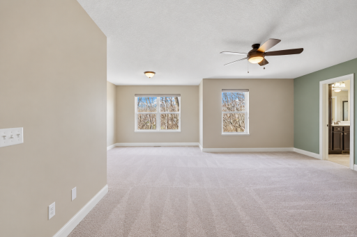 Expansive primary suite features abundant natural light, neutral finishes, plush carpeting, a ceiling fan, and convenient access to the private ensuite bath, offering plenty of flexibility for a custom bedroom layout.