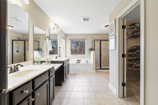 Spacious primary bath designed for comfort and convenience, featuring dual vanities, abundant cabinetry, a soaking tub, separate walk-in shower, tile flooring, and direct access to the walk-in closet. Multiple windows bring in beautiful natural light