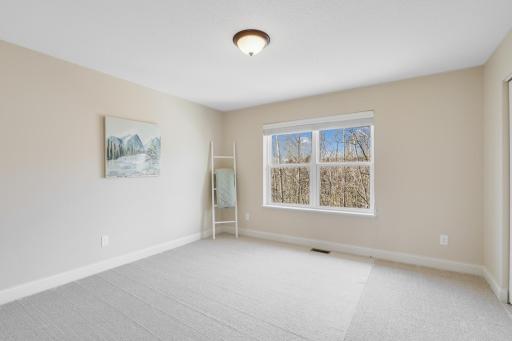 Bright and inviting upper-level bedroom features neutral finishes, plush carpeting, and a large window overlooking the wooded surroundings. Generous floor space offers flexibility for bedroom furnishings, a desk, or a cozy sitting area