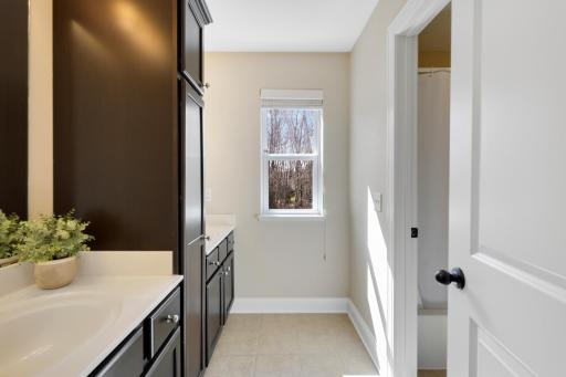 Bright full bathroom featuring rich cabinetry, generous counter and storage space, tile flooring, and a separate shower area. Natural light adds to the fresh, inviting feel