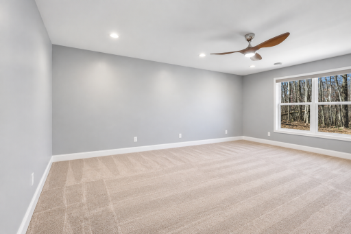 Spacious lower-level bedroom featuring large windows that bring in abundant natural light and peaceful wooded views. Generous proportions offer plenty of flexibility for bedroom furniture, a sitting area, or workspace.