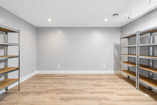 Versatile lower-level craft and storage room featuring durable flooring, recessed lighting, and ample shelvingâan ideal space for hobbies, projects, organization, or additional household storage.