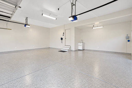 Spacious, well-maintained garage featuring durable epoxy flooring, bright overhead lighting, convenient utility sink, and plenty of open space for vehicles, storage, or projects.