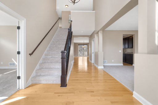 A welcoming two-story foyer showcases warm hardwood floors, an open staircase, soaring ceilings, and an airy layout filled with natural light. The open sightlines connect the entry to the dining area and kitchen, creating an inviting flow throughout
