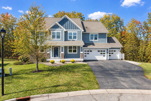 Beautiful two-story home featuring inviting curb appeal, a welcoming covered front porch, stone accents, and an attached three-car garage. Mature trees and a wooded backdrop provide a scenic setting