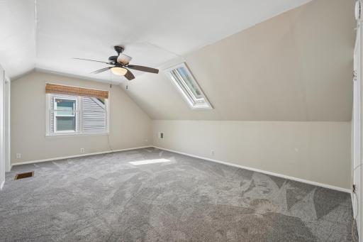 Upper bedroom with vaulted ceiling, ceiling fan, and skylight