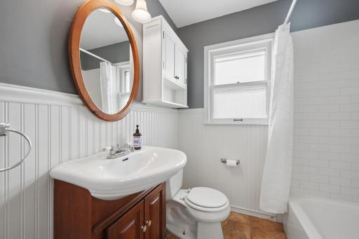 Bath detail â wood vanity, white wainscoting, and full tub surround