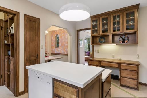 Kitchen with glass-front upper cabinets, built-in desk, and arched opening to the breakfast nook.