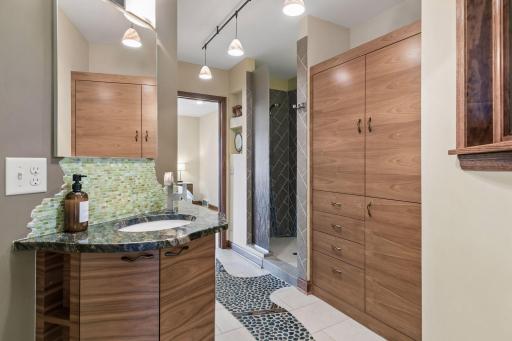 Primary bath by Otogawa-Anschel Design+Build with walnut built-ins, live-edge granite vanity, and river-stone floor path.