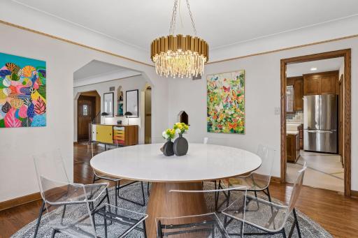 Dining room with gold and crystal chandelier, arched opening, and view into the kitchen.