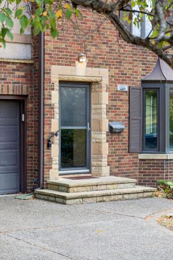 Front entrance with cut stone surround, brick facade, and glass storm door.