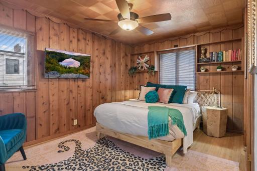 Upper-level 2nd bedroom with knotty pine walls and ceiling, built-in shelving, and ceiling fan.