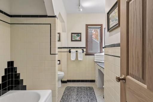 Upper hall bath view with original tile wainscot and black accent border.