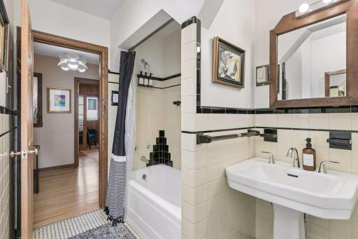 Upper hall bath with pedestal sink, tub and shower, and black tile trim.