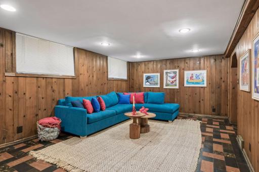Lower-level family room with knotty pine paneling and patterned tile floor.