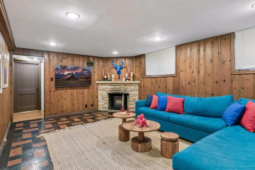 Lower-level family room with knotty pine walls, stone fireplace, and recessed lighting.