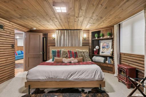 Lower-level bedroom with log cabin walls, plank ceiling, and built-in shelving.