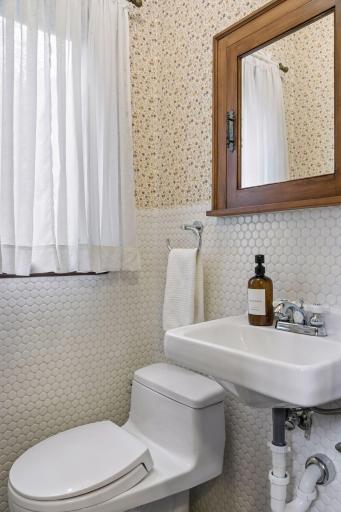 Powder room with pedestal sink, hexagon tile wainscot, and patterned vintage wallpaper.