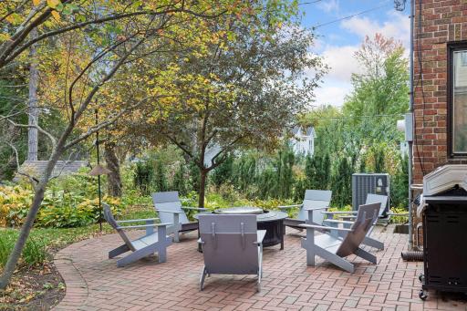 Herringbone brick patio surrounded by perennial gardens and mature trees.
