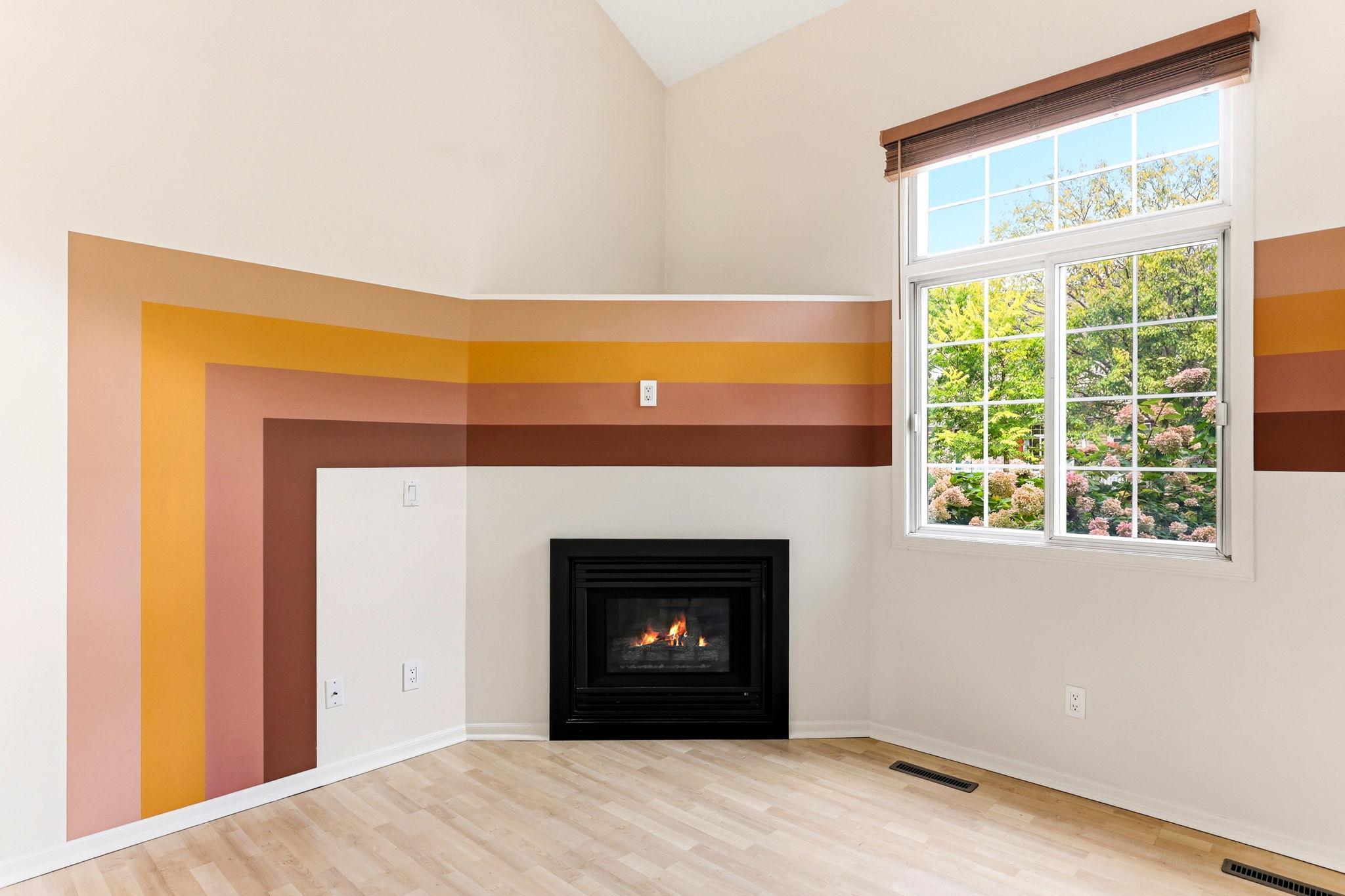 Natural light pours through the large window, highlighting the professionally painted custom accent wall and corner fireplace, creating a warm and inviting focal point in the main living area.