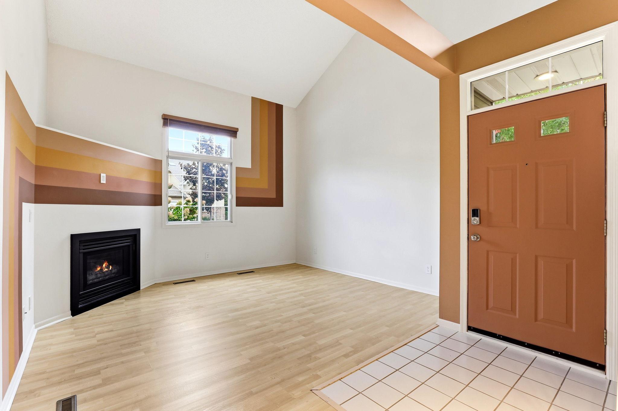 Step inside to a striking living room with vaulted ceilings, durable wood-look laminate flooring, and a cozy corner fireplace. The space features fresh, professional paint that adds architectural flair.