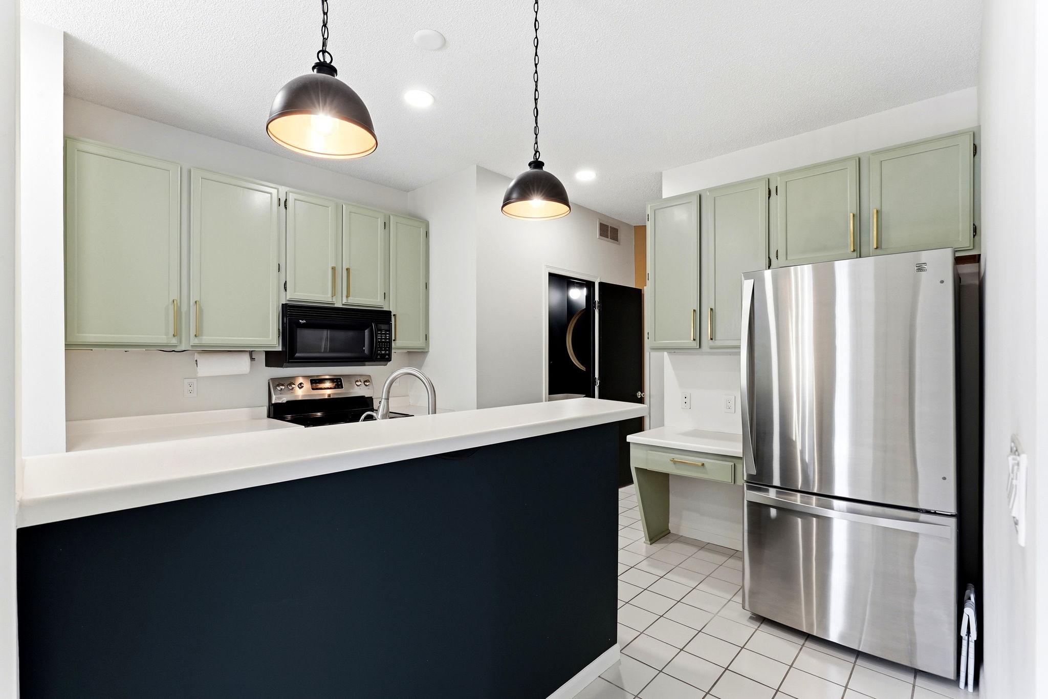 Complete with a convenient breakfast bar and modern pendant lighting, this kitchen features beautifully painted cabinetry and a stainless refrigerator, combining style with everyday function.