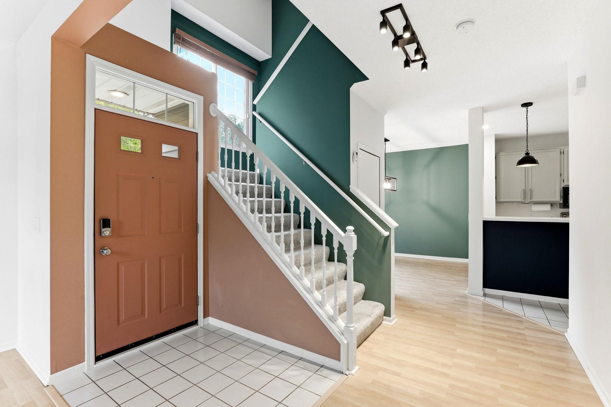 A tiled entryway transitions smoothly into wood-look laminate flooring. The open staircase and professionally painted accent walls enhance the architectural interest and seamless flow into the kitchen.