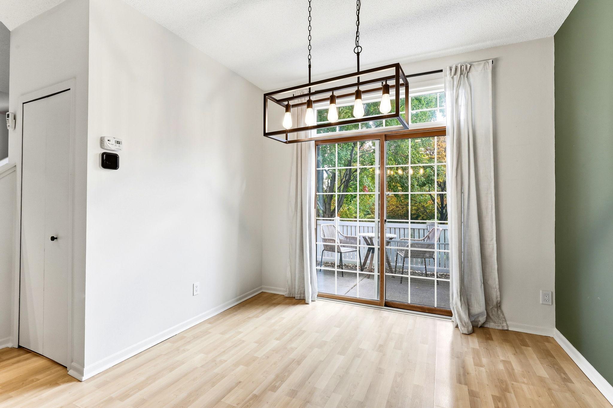 Wood-look laminate flooring continues through the dining area, which is anchored by a stylish lighting fixture and bathed in natural light from the expansive patio doors.