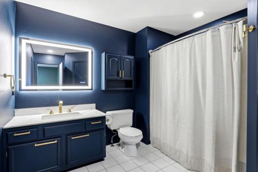 This beautifully updated bathroom boasts rich blue paint, a stylish new illuminated mirror, fresh countertops, and elegant new gold faucets and accents that elevate the entire space.