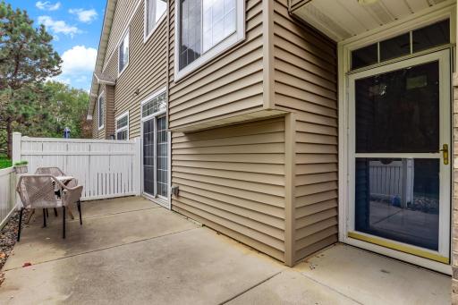 Step around to the private side patio, enclosed by a white privacy fence. This outdoor living space offers direct access to the home interior through both a sliding glass door and the main entry door.