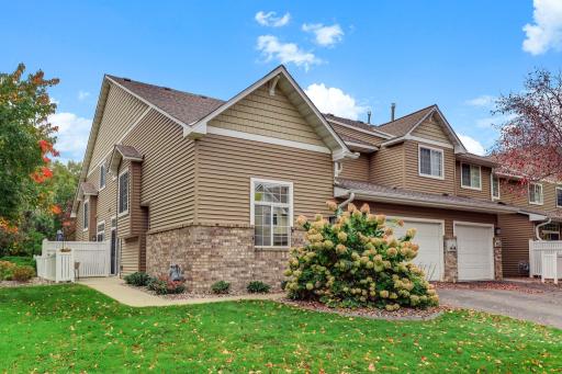 Welcome to this beautifully maintained end-unit townhome. The exterior features a classic mix of tan siding and brick accents, complemented by mature landscaping and a convenient attached garage.