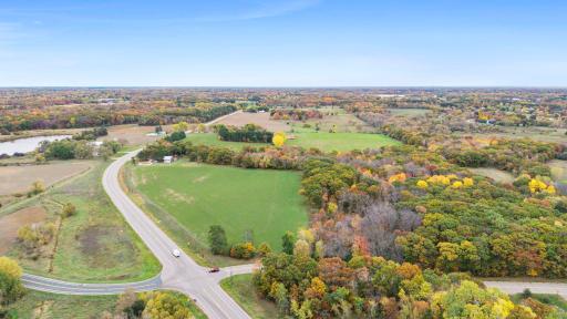 A sweeping aerial view highlights the property's road frontage, open fields, and wooded areas, offering an excellent perspective of the land's layout