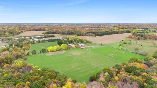 Expansive green fields stretch toward the existing agricultural improvements, showcasing the property's substantial open acreage and established farming setting