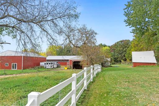 White fencing and established pasture areas surround the agricultural outbuildings, providing a functional setup for horses and livestock
