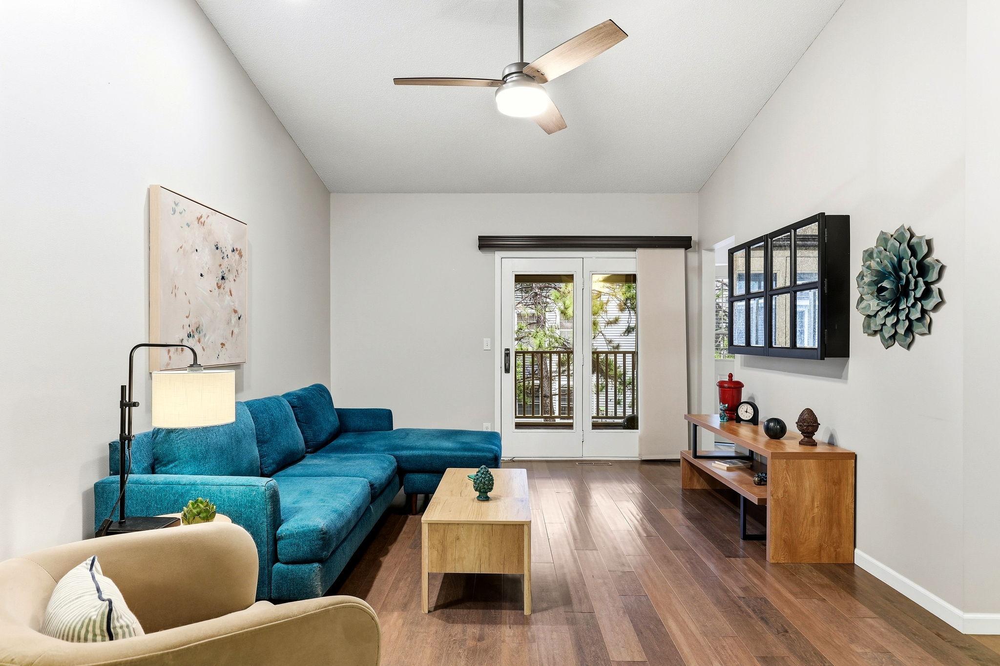 Another view of the spacious living room showcasing vaulted ceilings, wood flooring, a ceiling fan, and French doors leading to the private balcony.