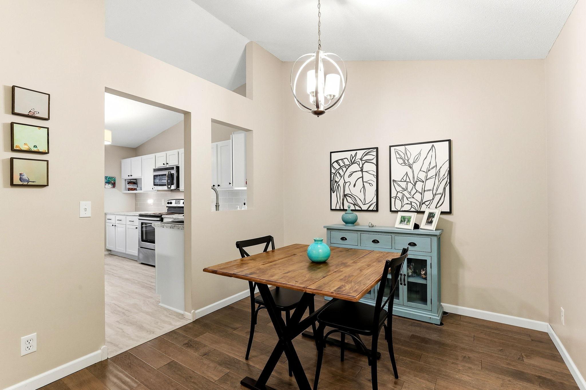 Another view of the dining area highlighting the vaulted ceiling, modern lighting, wood flooring, and convenient pass-through to the kitchen.
