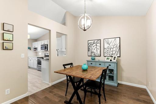 Another view of the dining area highlighting the vaulted ceiling, modern lighting, wood flooring, and convenient pass-through to the kitchen.