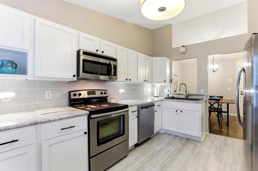 Updated kitchen featuring white cabinetry, tile backsplash, LVP flooring, stainless steel appliances, and a convenient pass-through to the dining area.