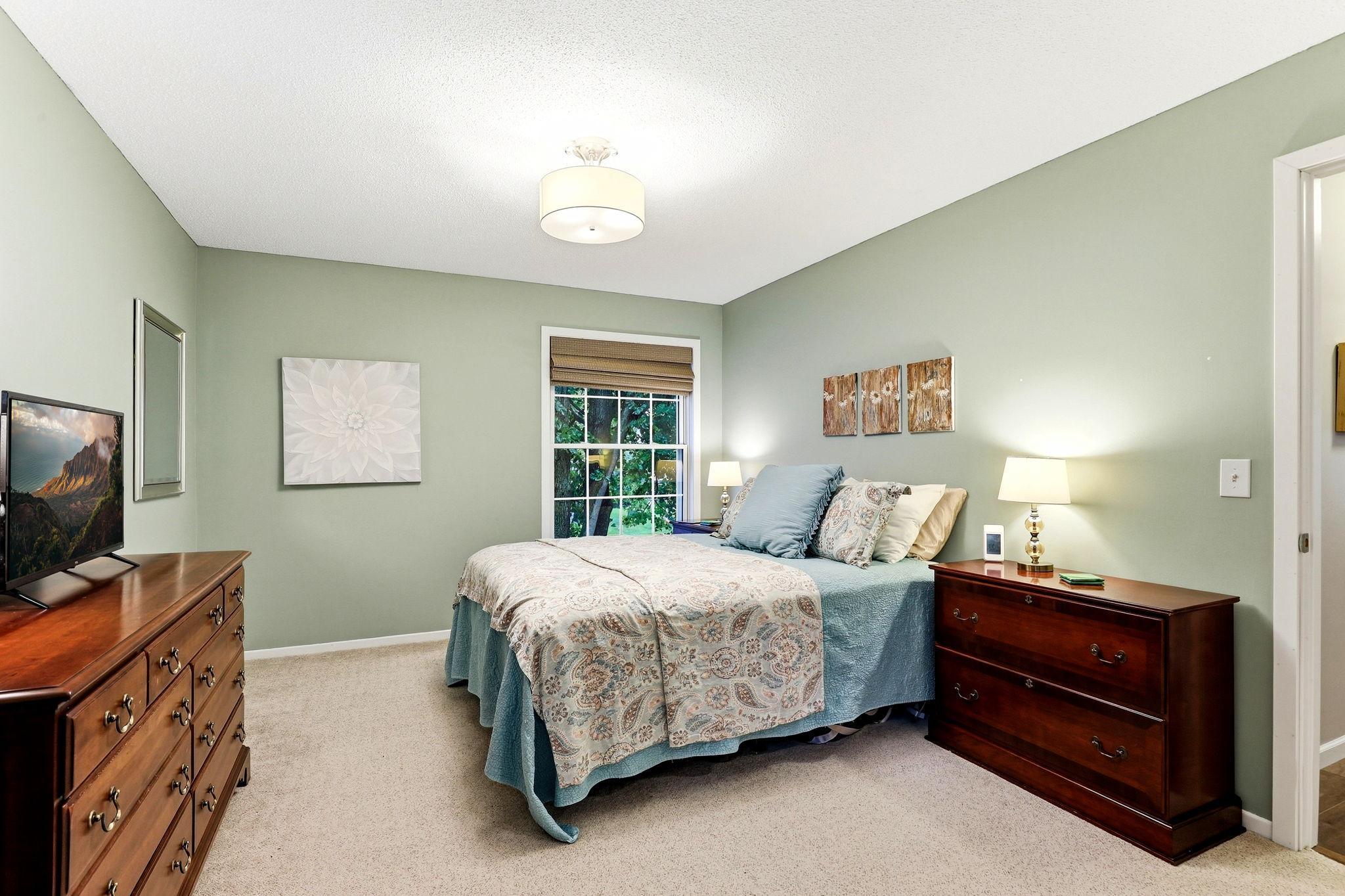 Another view of the spacious primary suite, featuring soft carpeting, natural light, and convenient access to the private ensuite bath and walk-in closet.