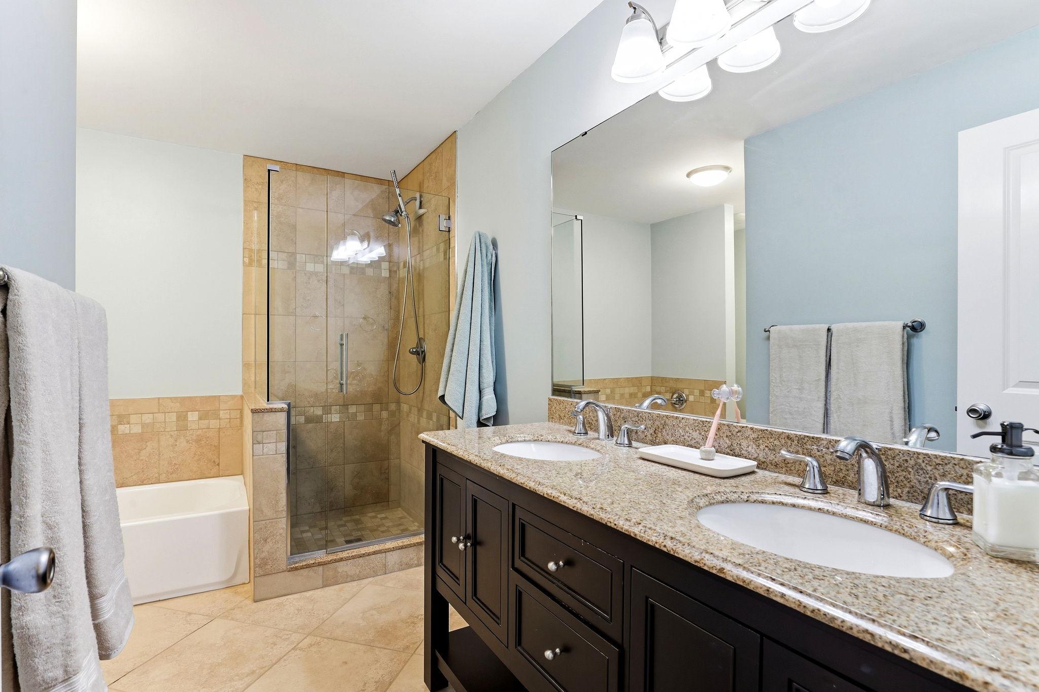 Full primary bath featuring a double-sink granite vanity, tiled walk-in shower with glass enclosure, separate soaking tub, and tile flooring.