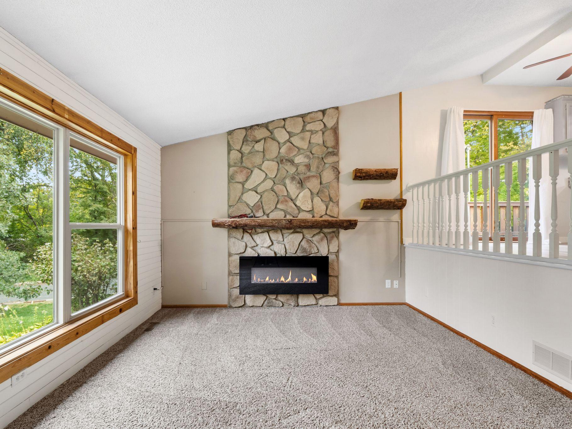 Bright and inviting, this main-level living room features a stunning stone fireplace, vaulted ceiling, plush carpeting, and large windows overlooking the beautiful outdoor setting. An open layout provides a comfortable and space for relaxing!